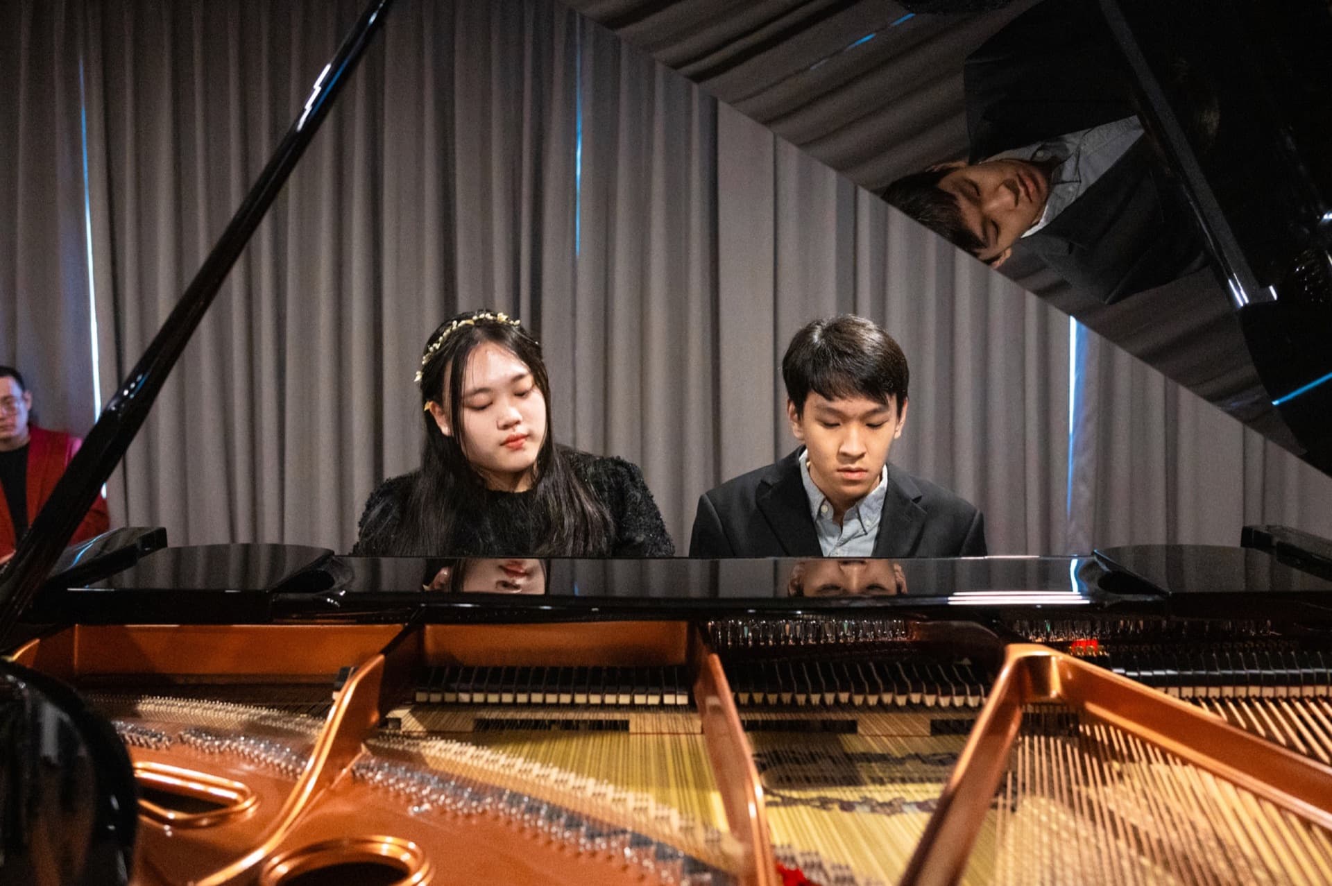 Two young pianists performing together at a grand piano.